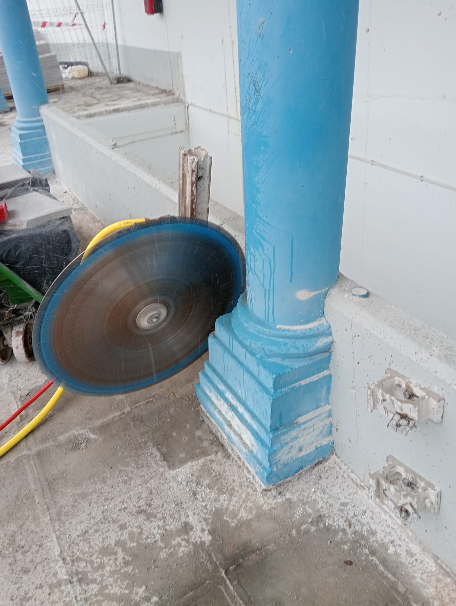Un trabajador utiliza una sierra giratoria para cortar una columna azul en una zona interior alicatada.