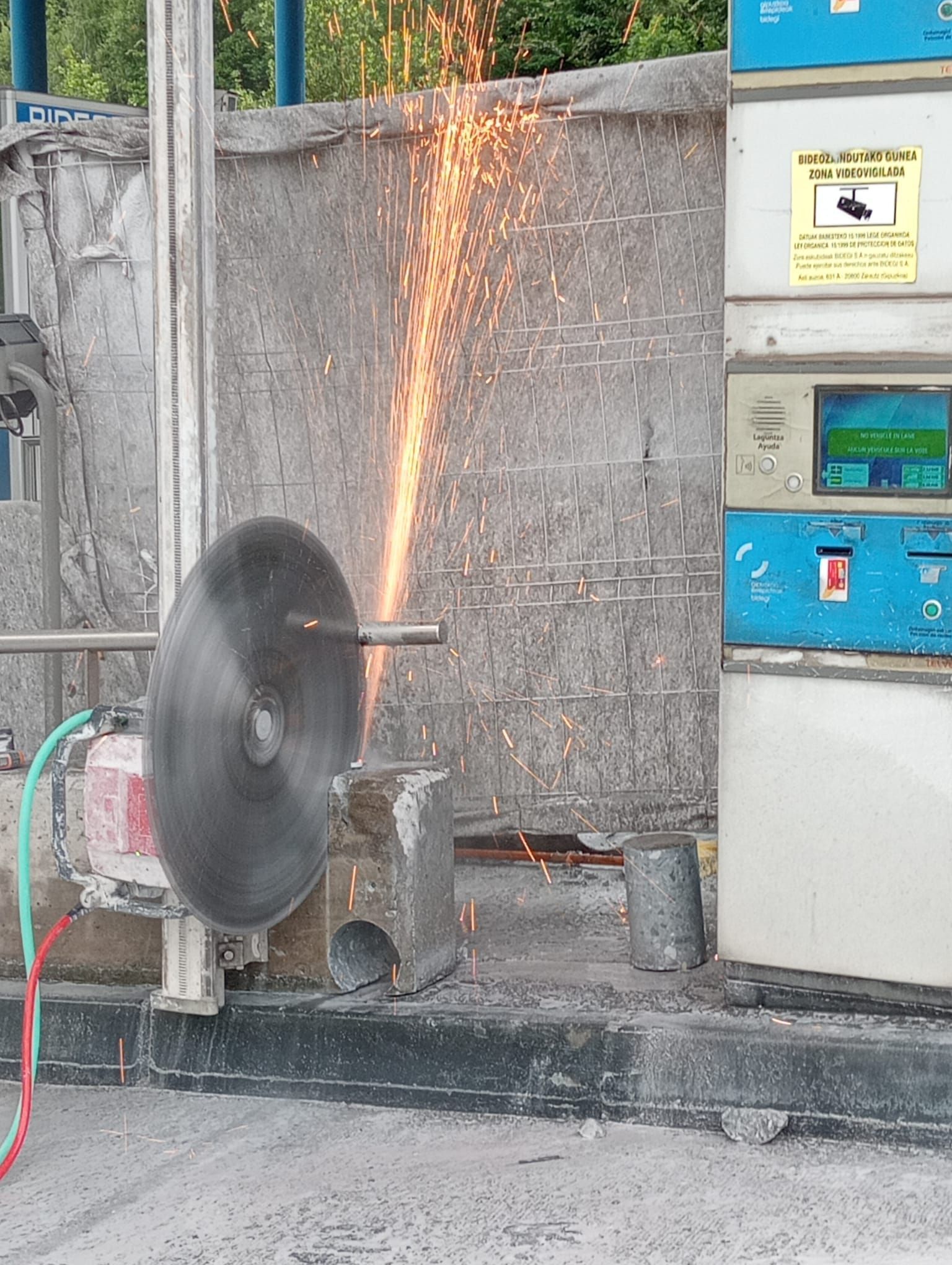 Sierra industrial cortando metal, lanzando chispas hacia arriba junto a un panel de control.