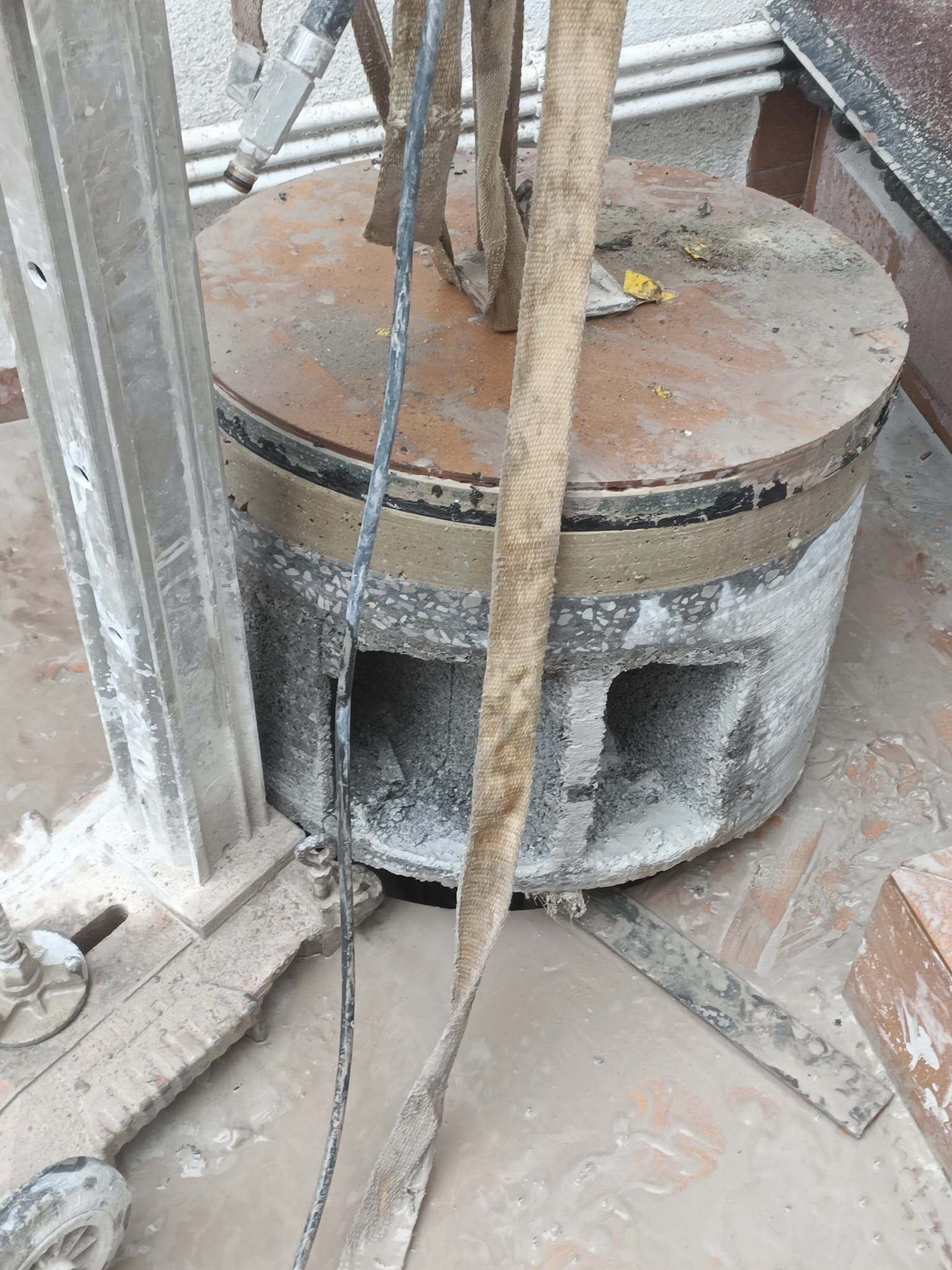 Estructura cilíndrica de hormigón con tapa metálica oxidada y cables colgantes en una obra en construcción.