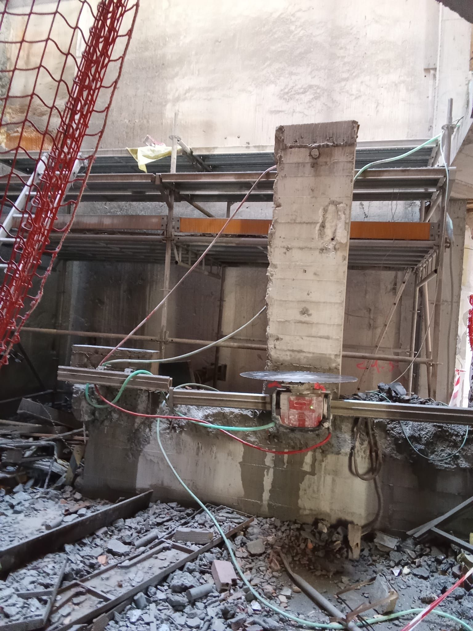 Obra en construcción con cimientos de hormigón, andamios, cables y una columna de soporte central en reparación.