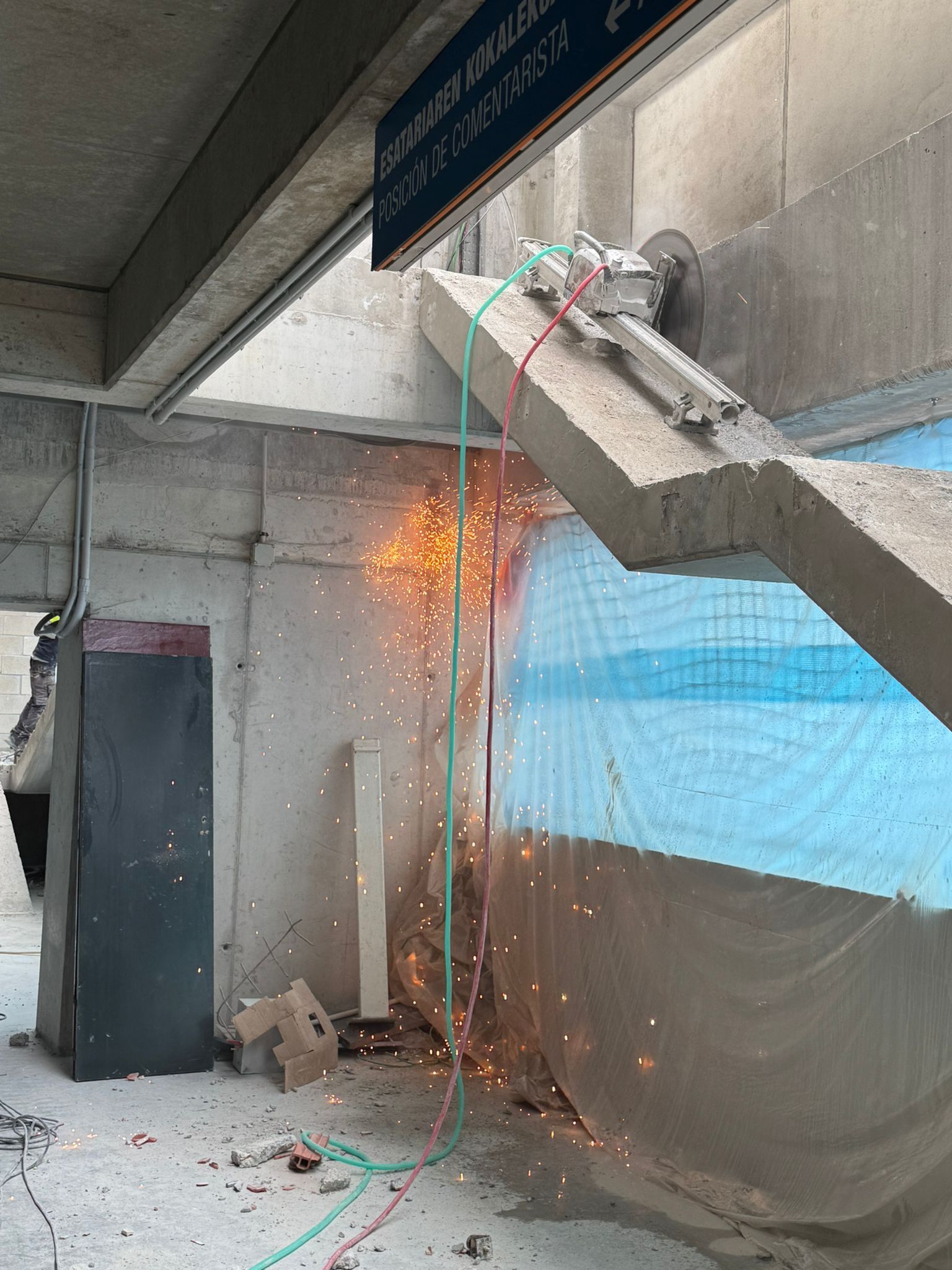 Un trabajador corta hormigón con una amoladora; saltan chispas en el interior, cerca de una pared y una puerta.