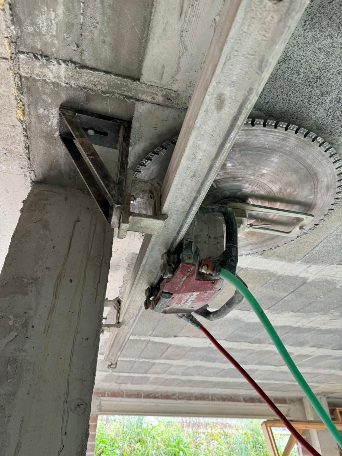 Amoladora angular cortando una viga de hormigón en altura, con polvo y cables en un entorno de construcción.