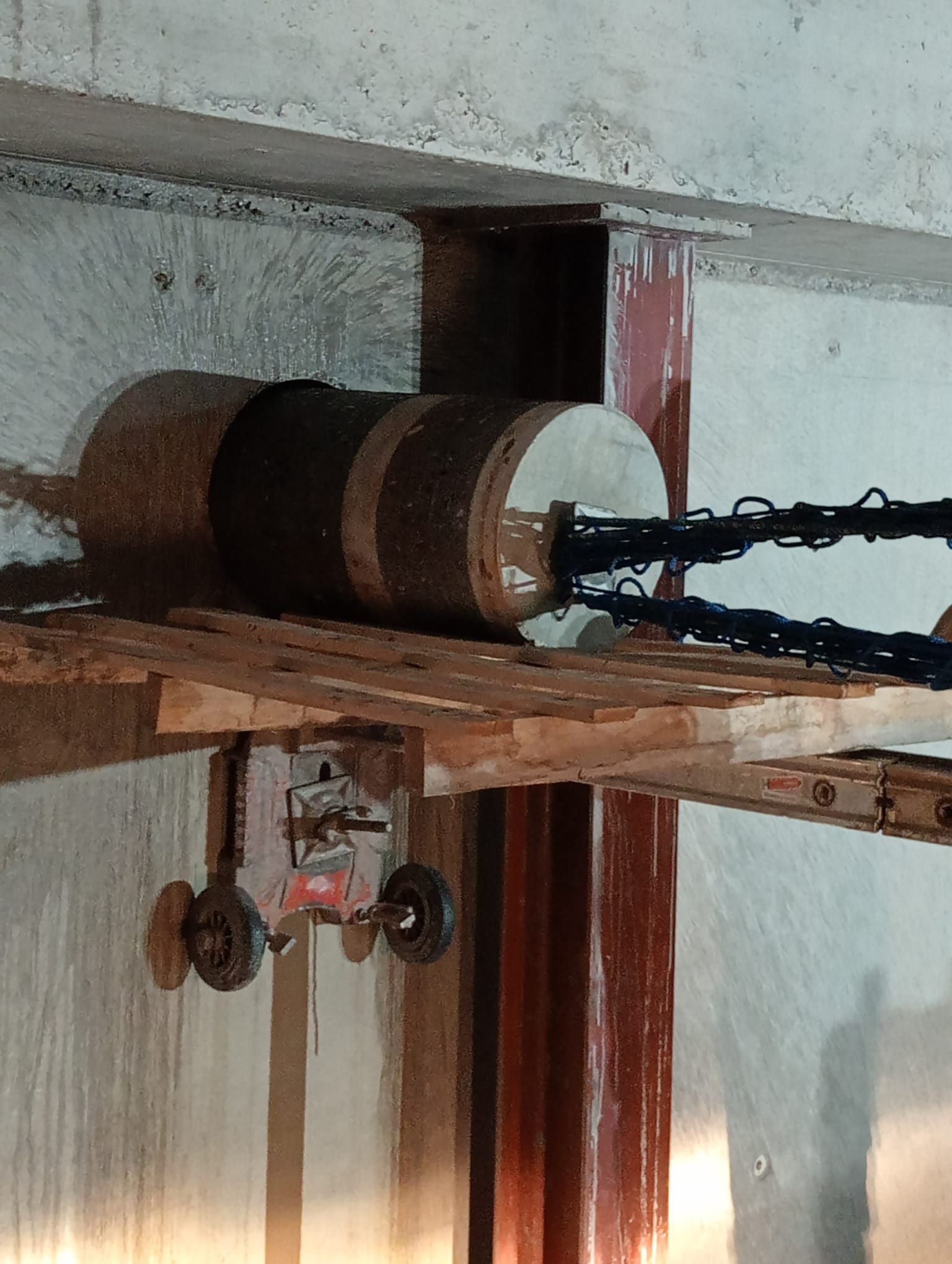 Polea de madera con cadena montada debajo de una viga en un área de techo que parece un taller.