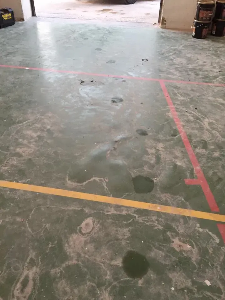 Suelo de hormigón verde con manchas de aceite, líneas pintadas de rojo y amarillo, en una puerta.