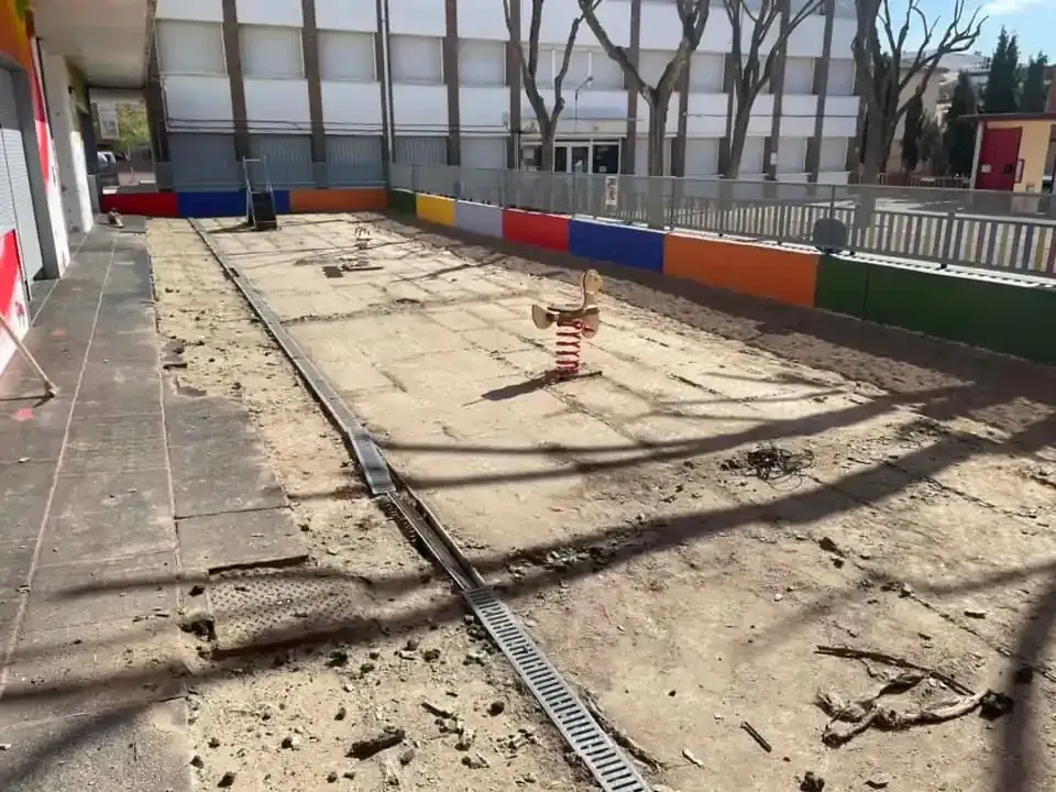 Parque infantil con superficie de arena, borde colorido y corredera con resortes.