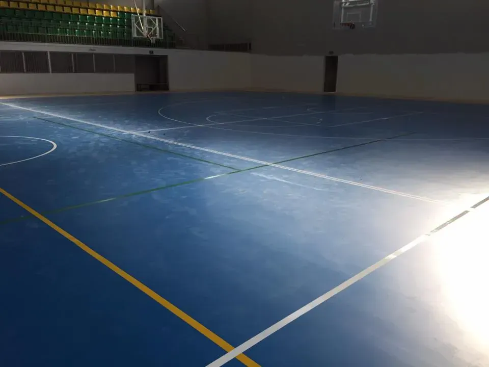 Cancha de baloncesto azul con líneas blancas y amarillas, vacía con gradas al fondo.