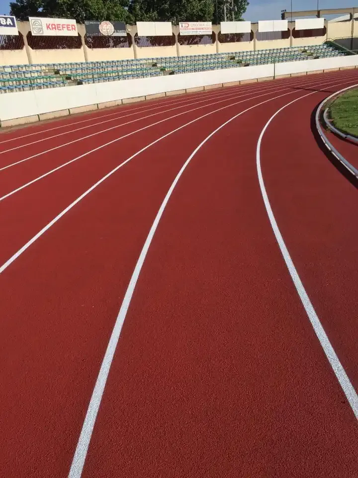 Pista de carreras roja con marcas de carril blancas y asientos tipo estadio al fondo.