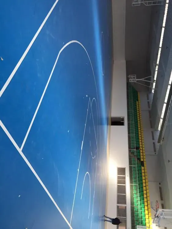 Cancha de baloncesto azul con líneas blancas; una persona está de pie junto a la pared.