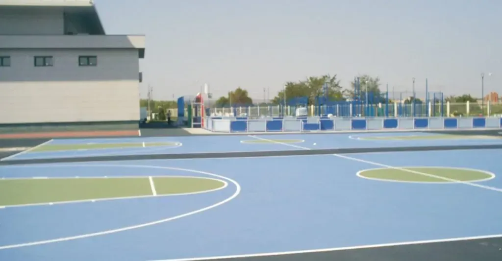 Cancha de baloncesto al aire libre con pintura azul y verde, adyacente a un edificio.