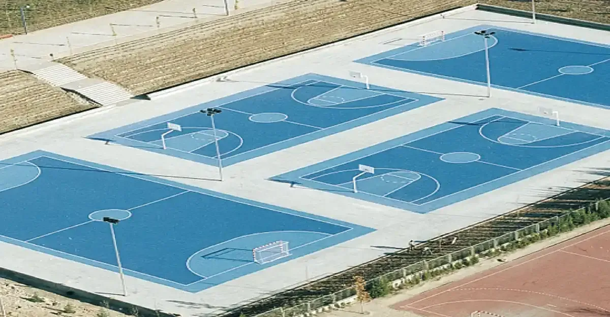 Canchas de balonmano azules en un entorno de parque al aire libre con iluminación, rodeadas de pavimento de color claro