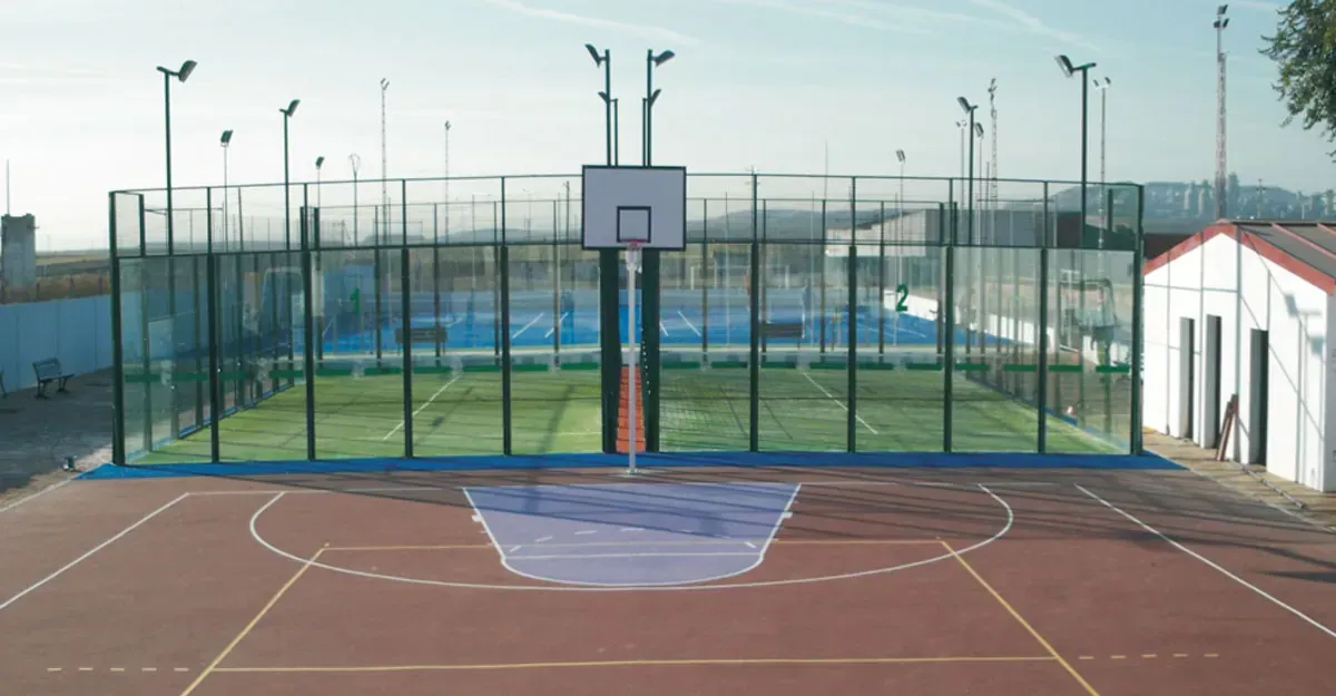 Complejo deportivo al aire libre con cancha de baloncesto en primer plano, pistas de pádel detrás