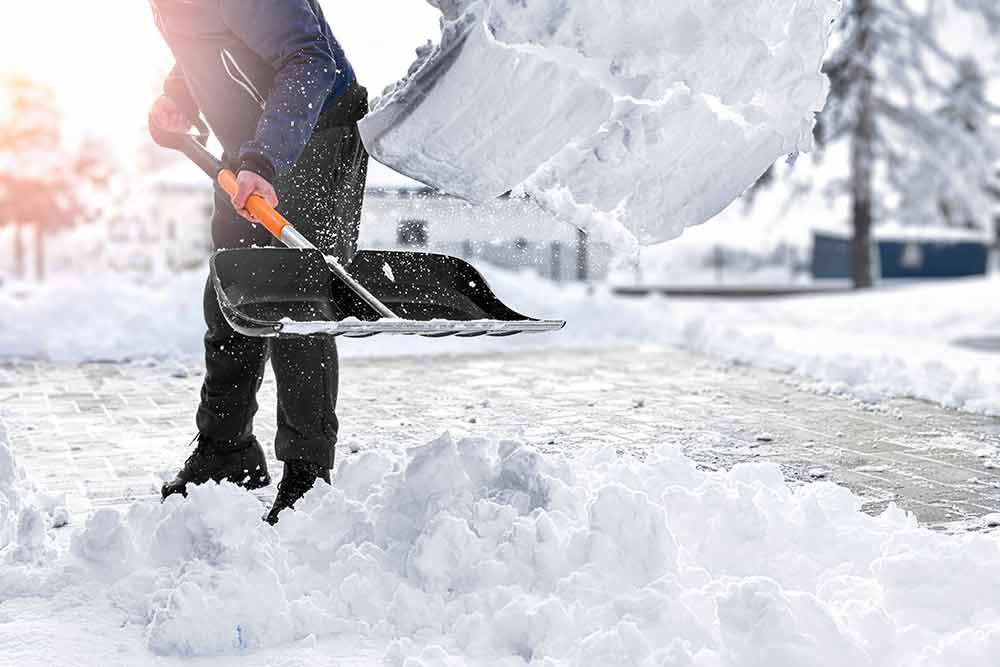 Eine Person schaufelt mit einer Schaufel Schnee von einem Gehweg.