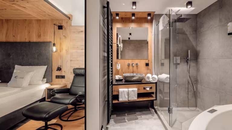 Ein Hotelzimmer im industrial Design mit einem Bett, einem Leder-Sessel und einem modernen Badezimmer