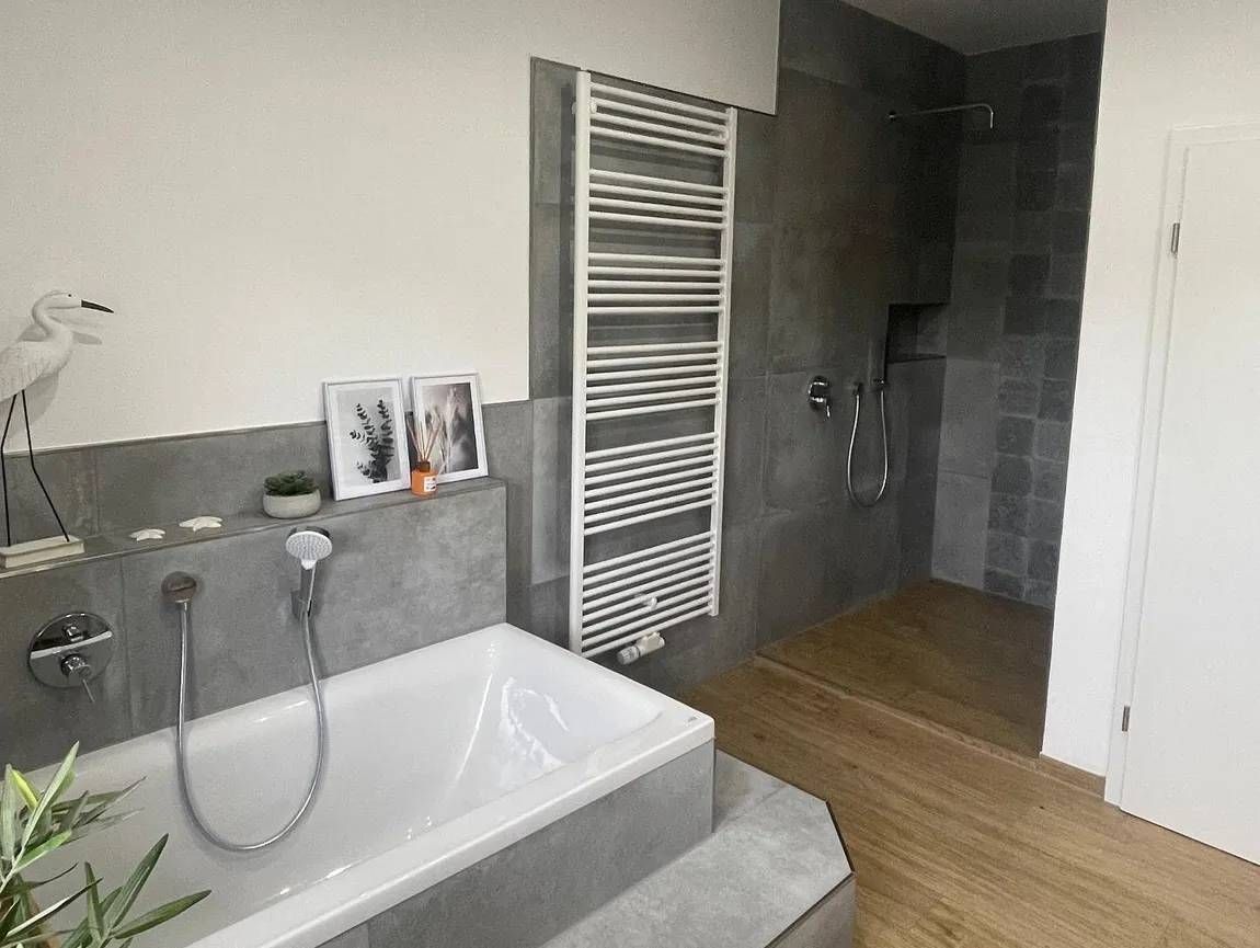 Ein grau gefliestes Badezimmer mit Badewanne und Dusche.