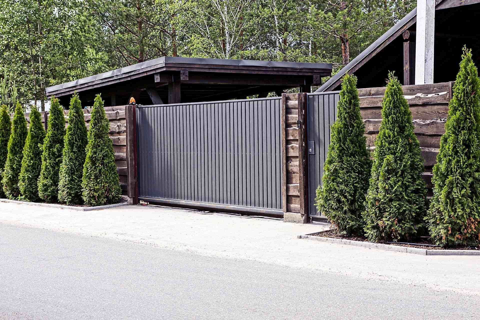 Uma cerca com um portão deslizante e árvores na frente dela.