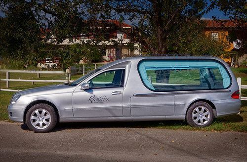 Un coche fúnebre plateado está estacionado al costado de la carretera.