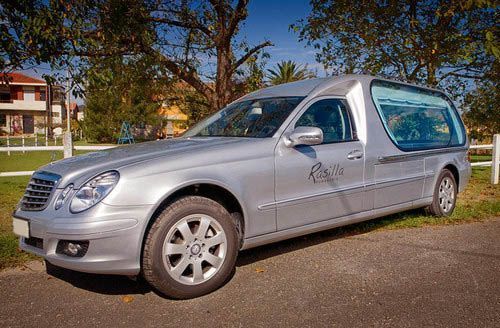 Un coche fúnebre plateado está estacionado al costado de la carretera.