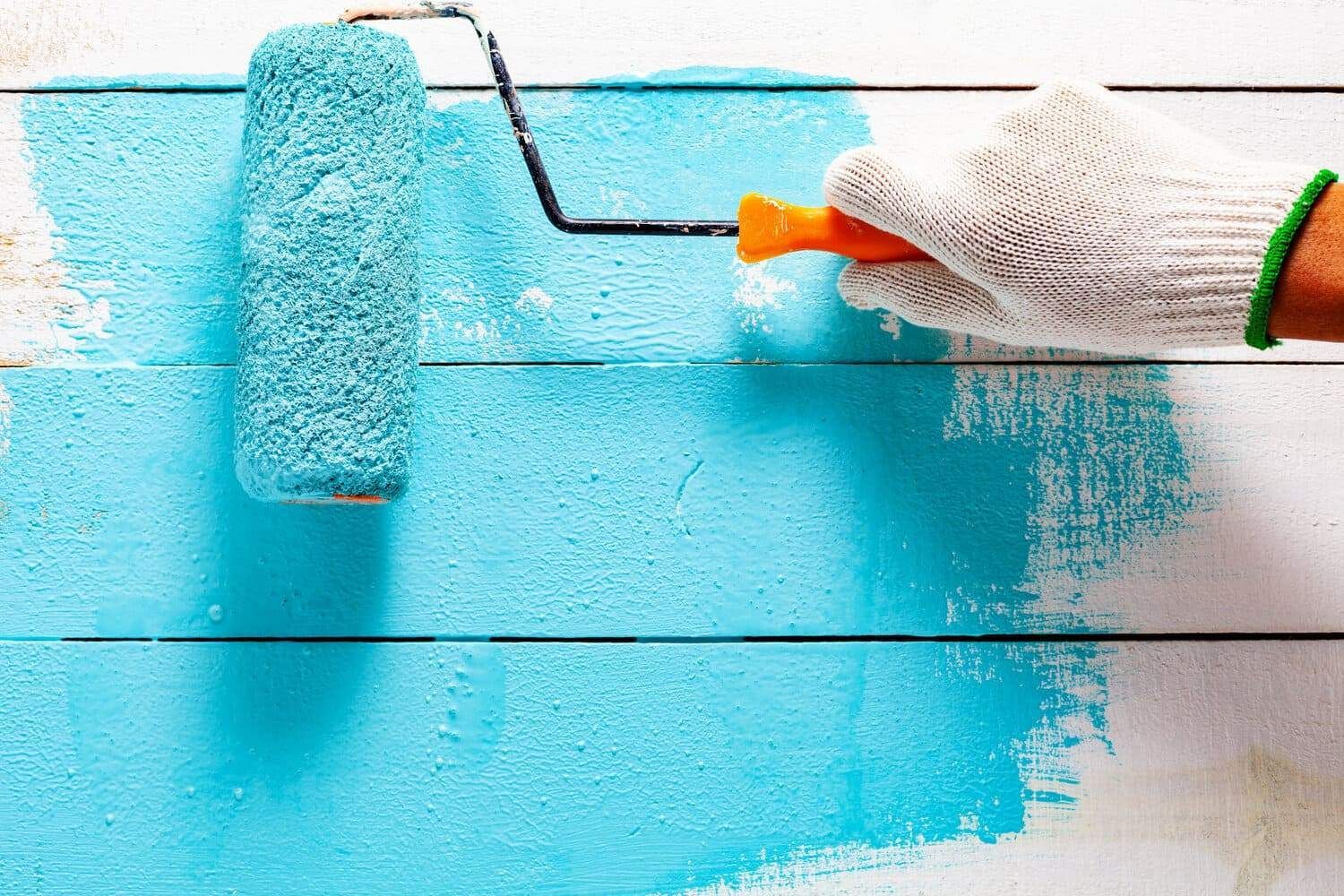 Una persona está pintando una pared de madera con un rodillo de pintura azul.