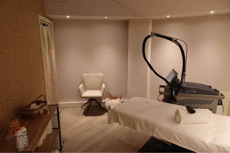 Ein Behandlungsraum mit Massageliege, Drehstuhl und medizinischer Ausrüstung für eine Hautbehandlung.
