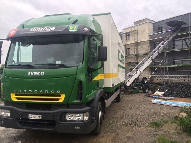 Grün-weißer Umzugswagen, der in der Nähe eines Gebäudes geparkt ist. Ein Aufzug führt zum Gebäude.