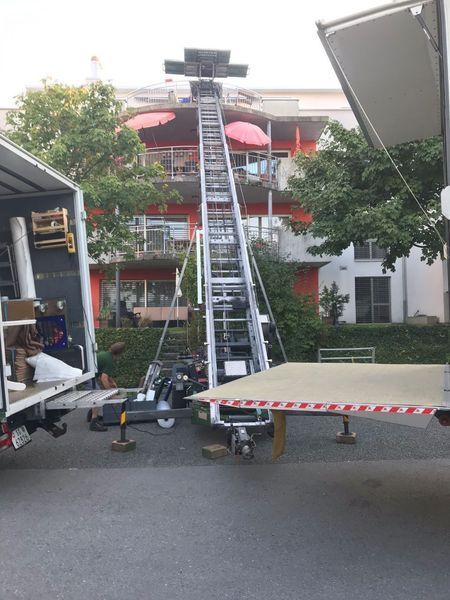 Ein Umzugswagen entlädt Möbel mithilfe einer ausfahrbaren Hebebühne auf einen hohen Balkon.
