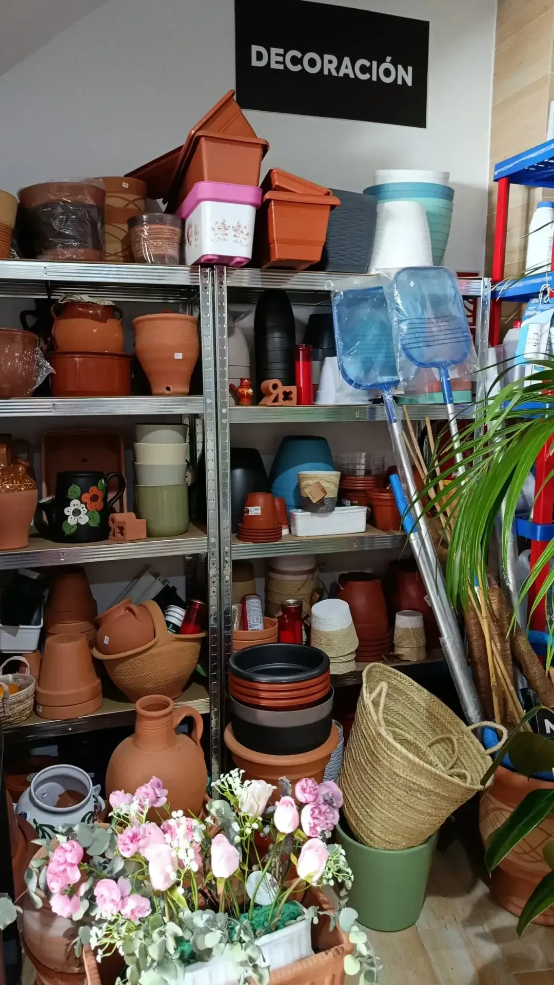 Estantes llenos de macetas de terracota, jardineras y artículos decorativos en una tienda etiquetada 
