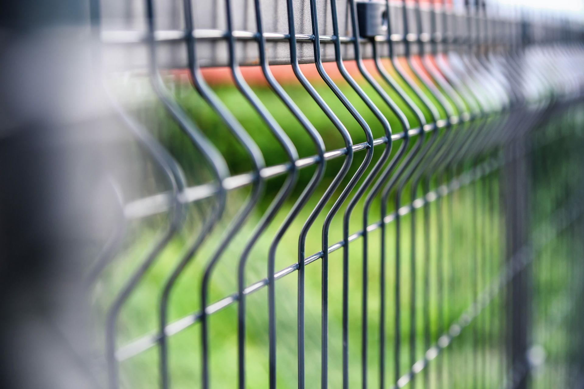 Clôture en grillage vert foncé avec pelouse verte en arrière-plan.