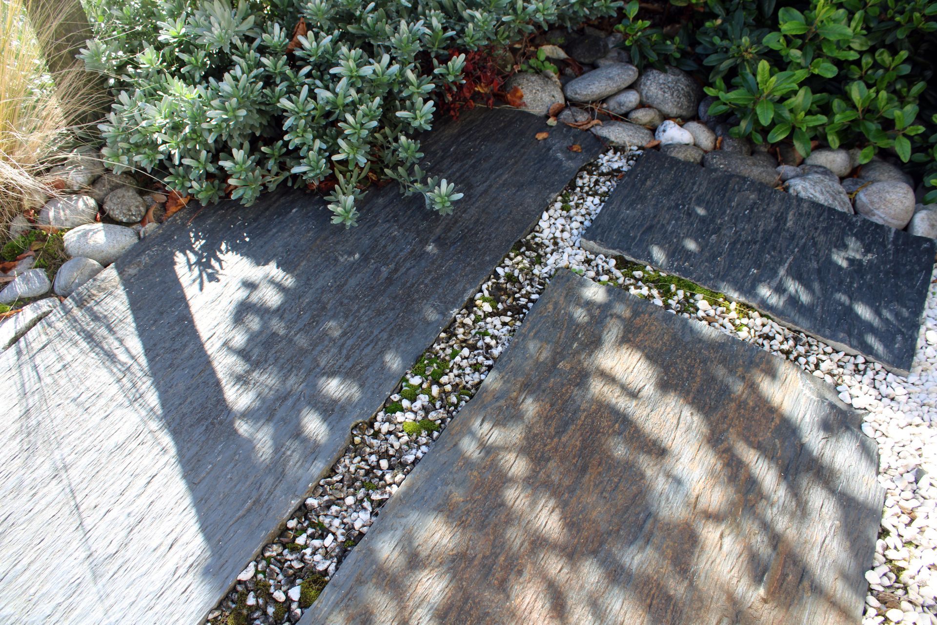 Allée de pierres traversant un jardin, bordée de galets blancs et de plantes.
