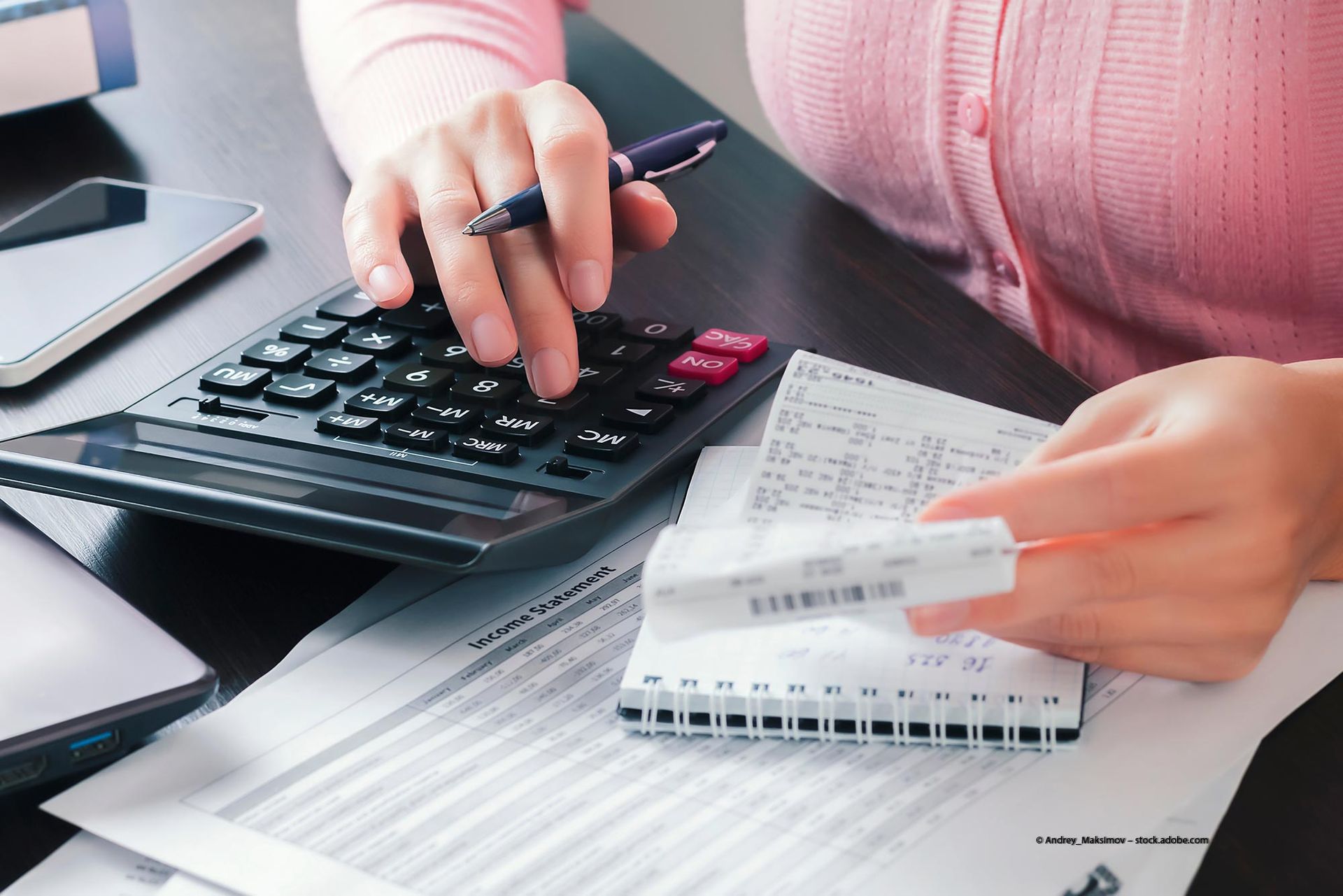 Zwei Personen analysieren in einem Büro mit einem Taschenrechner und einem Laptop Finanzdaten.
