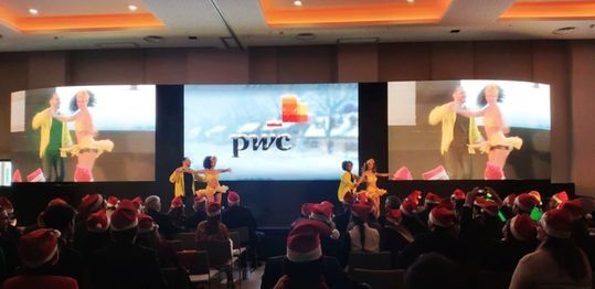 Un grupo de personas está sentada frente a una pantalla grande en una fiesta de Navidad.