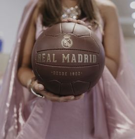 Una mujer con un vestido rosa sostiene un balón de fútbol del Real Madrid.