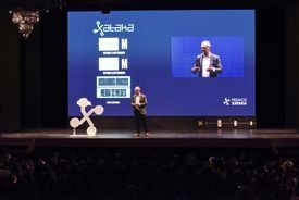 Un hombre está dando una presentación en un escenario frente a una pantalla grande.