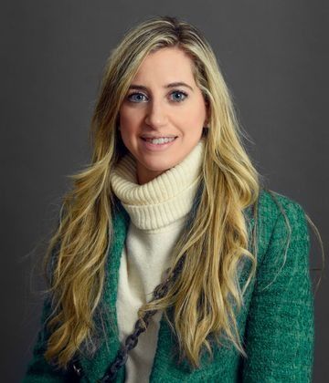La mujer lleva una chaqueta verde y un suéter blanco.
