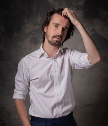 Un hombre con barba lleva una camisa blanca y pantalones azules.