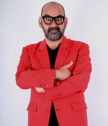 Un hombre calvo con barba lleva una chaqueta roja y gafas.