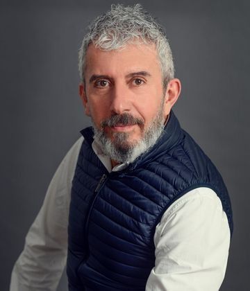 Un hombre con barba lleva un chaleco azul y una camisa blanca.