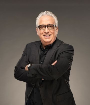 Un hombre con traje y gafas está de pie con los brazos cruzados.
