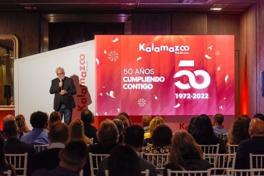 Un hombre está dando un discurso frente a una pantalla grande que dice 50 años cumpliendo contigo