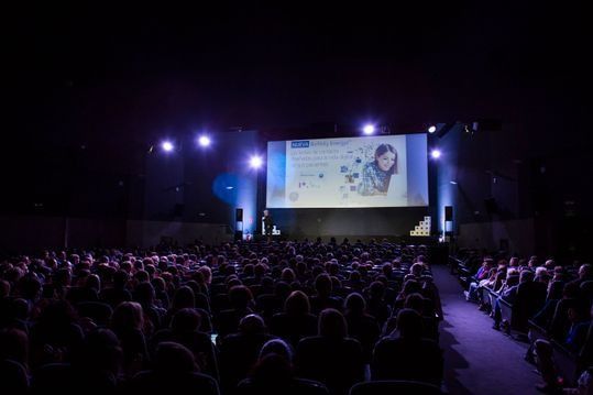 Una gran multitud de personas está viendo una presentación en un auditorio oscuro.