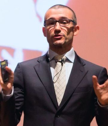 Un hombre con traje y gafas está de pie con los brazos cruzados.