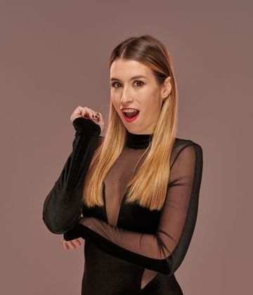 Una mujer con un vestido negro está de pie con los brazos cruzados y la boca abierta.