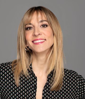 Una mujer con un vestido negro está de pie con los brazos cruzados y la boca abierta.