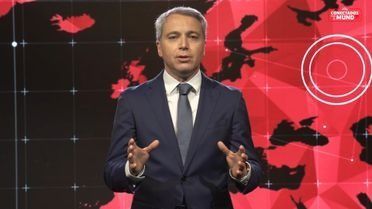 Un hombre con traje y corbata está parado frente a un mapa del mundo.