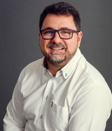 Un hombre que lleva gafas y una camisa blanca sonríe a la cámara.