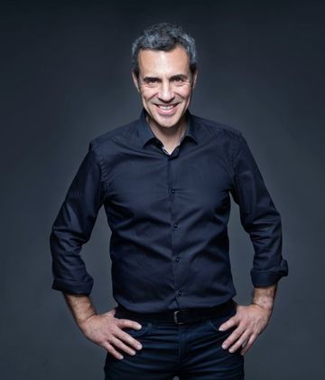 Un hombre con una camisa negra está de pie con las manos en las caderas y sonriendo.