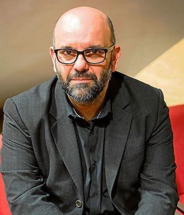 Un hombre con traje y gafas está de pie con los brazos cruzados.
