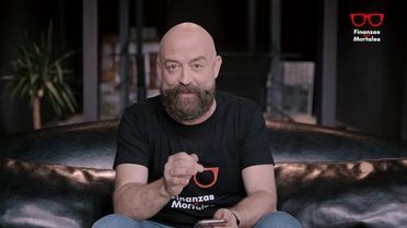 Un hombre calvo con barba está sentado en un sofá sosteniendo un teléfono celular.