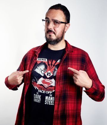 Un hombre con una camisa a cuadros roja señala su camisa.
