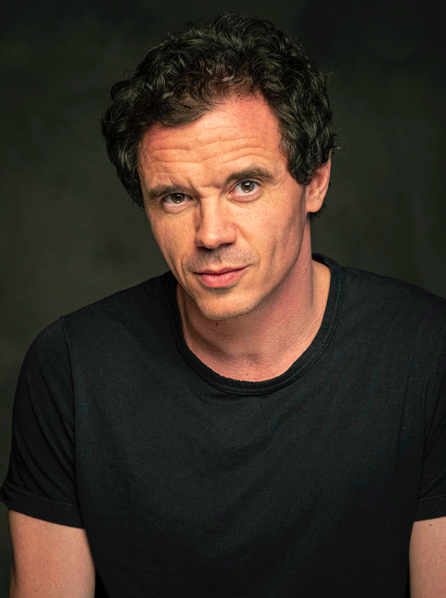 Un hombre con traje y gafas está de pie con los brazos cruzados.