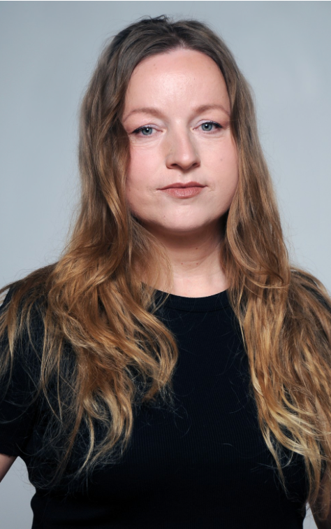 Una mujer con un vestido negro está de pie con los brazos cruzados y la boca abierta.